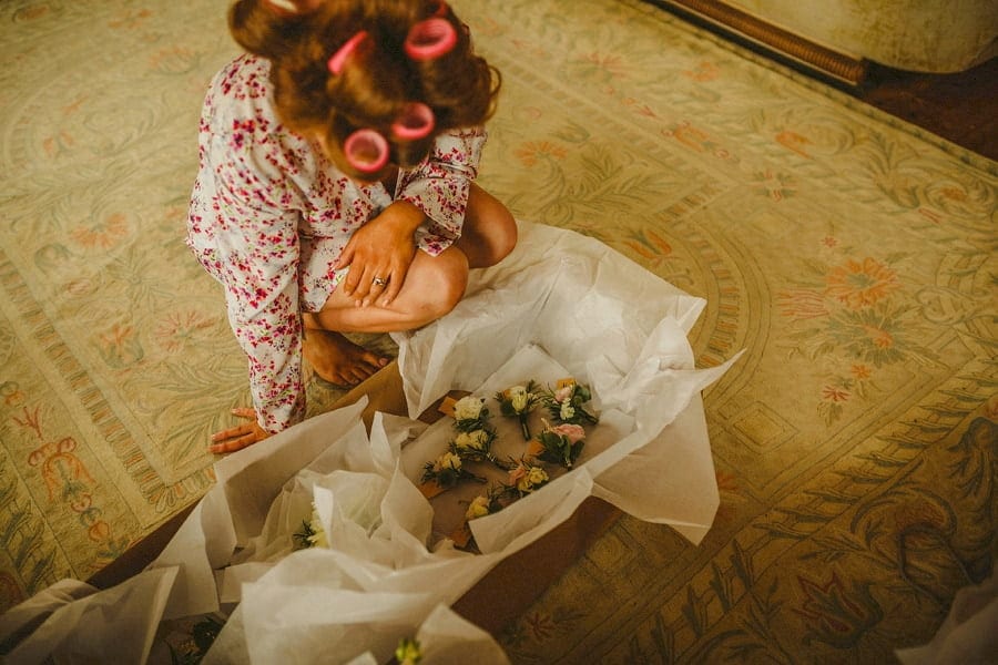 A bridesmaid bends down and looks at the box of bouquets on the floor