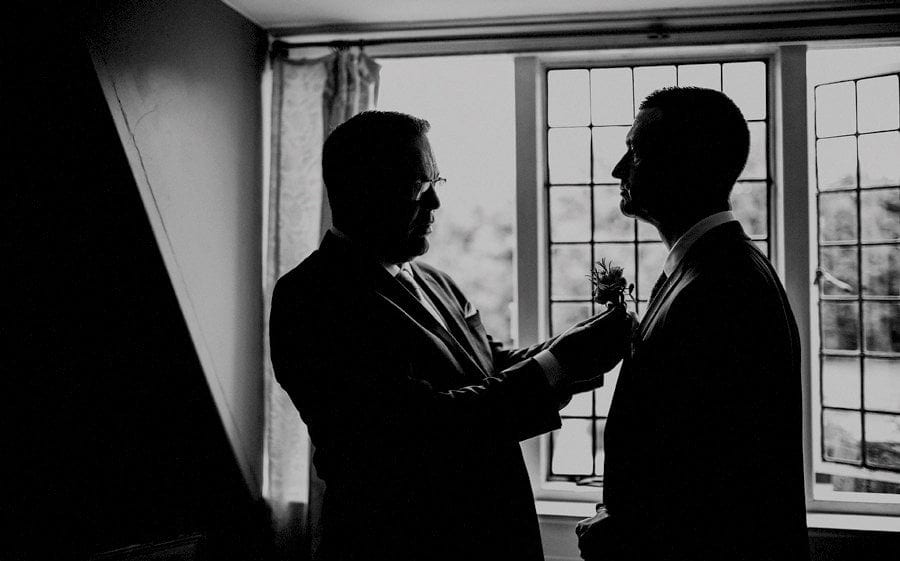 The best man places a flower on the lapel of the grooms suit