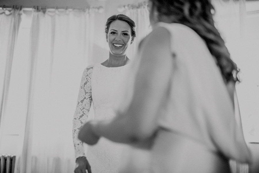 The bride smiles at a bridesmaid in the main bedroom at Voewood House in Norfolk