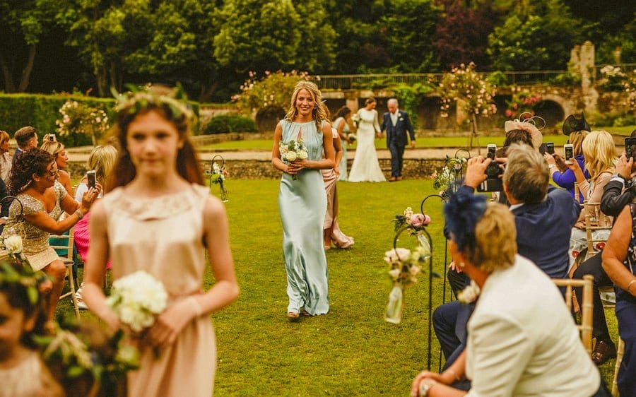 A bridesmaid and flower girls walk down the aisle of the outdoor ceremony at Voewood