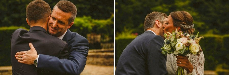 The bride and groom embrace a wedding guest at the end of the outdoor wedding ceremony at Voewood House in Norfolk