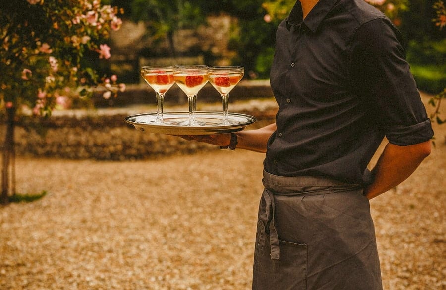 A waiter stands and holds a tray with champagne filled glasses
