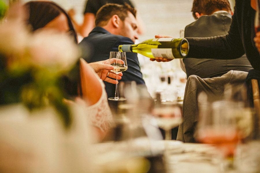 A waitress pours a glass of wine for a wedding guest who sits at the table in the marquee