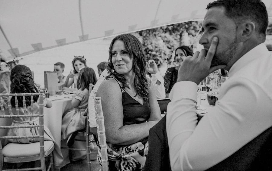 A wedding guest sat at the wedding table in the marquee smiles as she listens to a speech