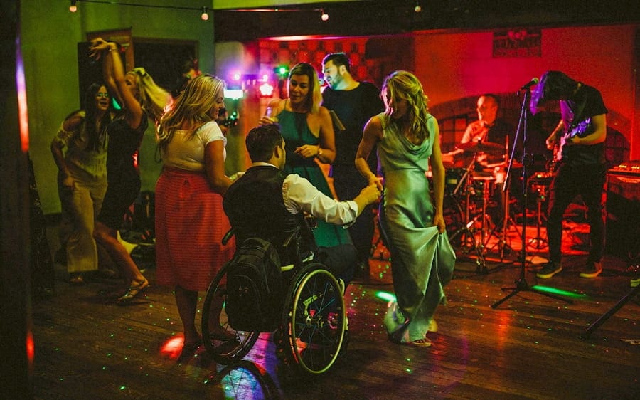 A man in a whell chair dances with a bridesmaid on the dancefloor at Voewood