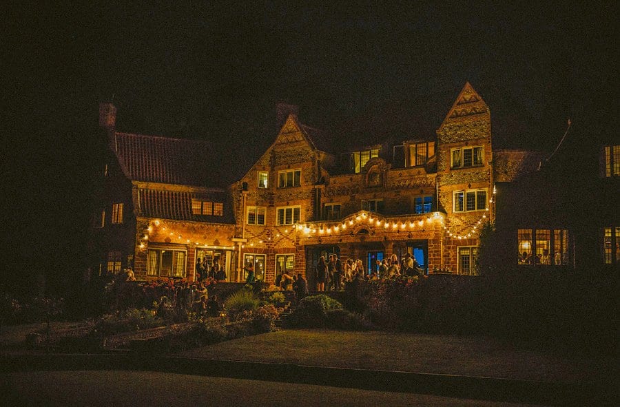 Wedding guests stand outside beautifully lit Voewood House at midnight