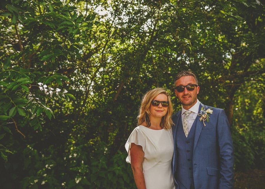 A portrait of the bride and groom in front of a large bush in the garden