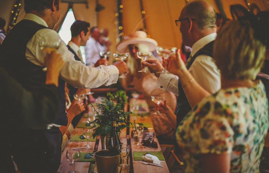 Champagne glasses are raised and people stand up in the tipi