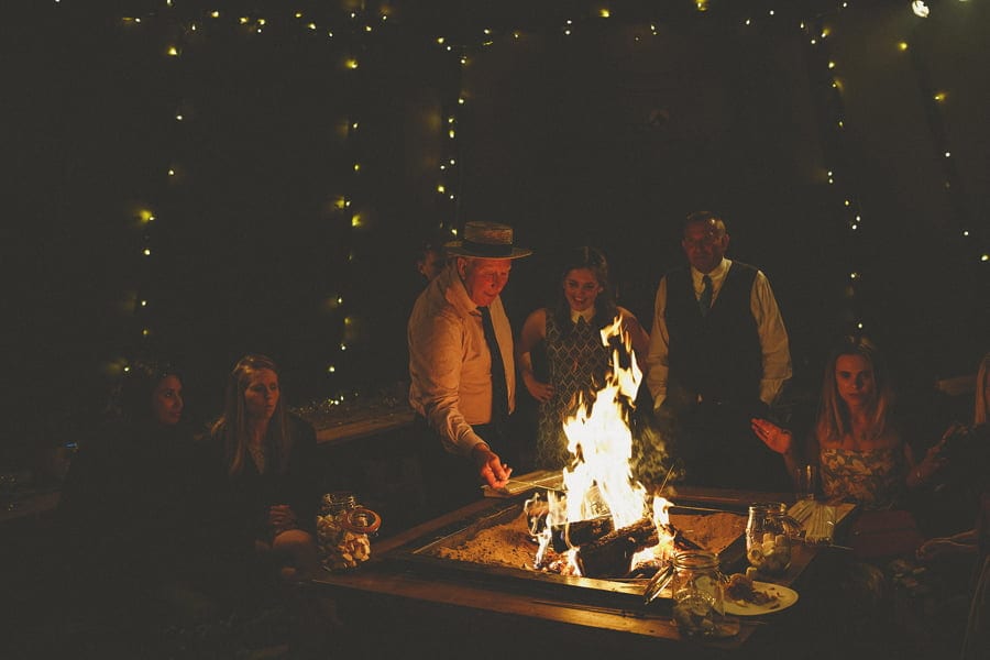 Wedding guests gather around the fire pit to toast marshmallows in the tipi