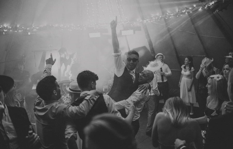 The groom is lifted in the air by the wedding guests on the dancefloor in the tipi