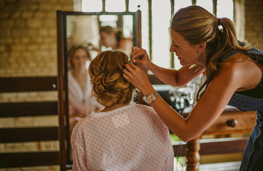 The hair stylist pins the right side of the brides hair as the bride looks in the mirror