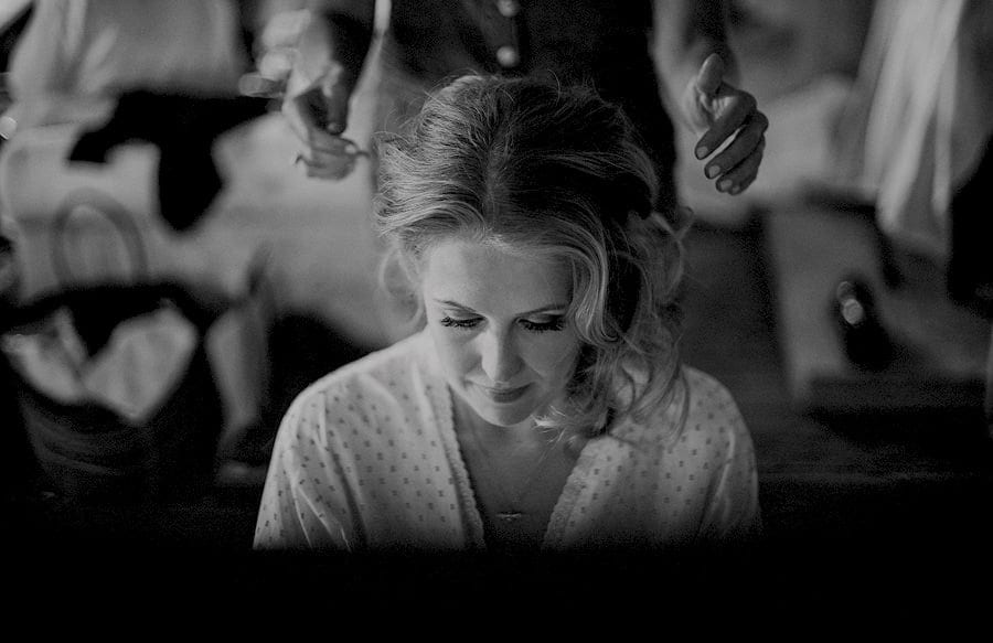 The bride looks down as the hair stylist shapes the brides hair in the old barn at Childerley