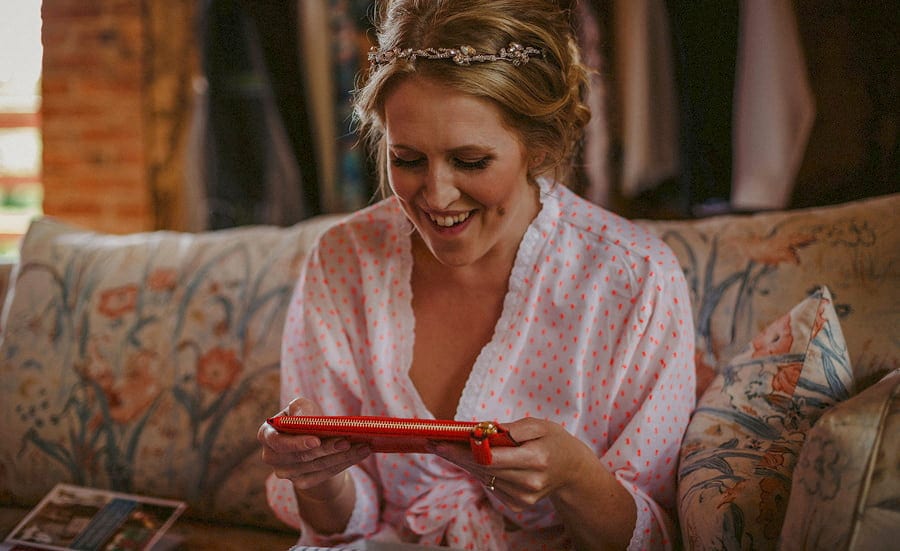The bride holds a red purse in both hands and smiles in the old barn