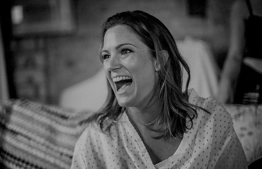 A bridesmaid laughs as she listens to her friend talk in the old barn