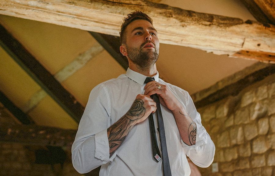 The bride's brother fastens his tie and looks in the mirror in the old barn