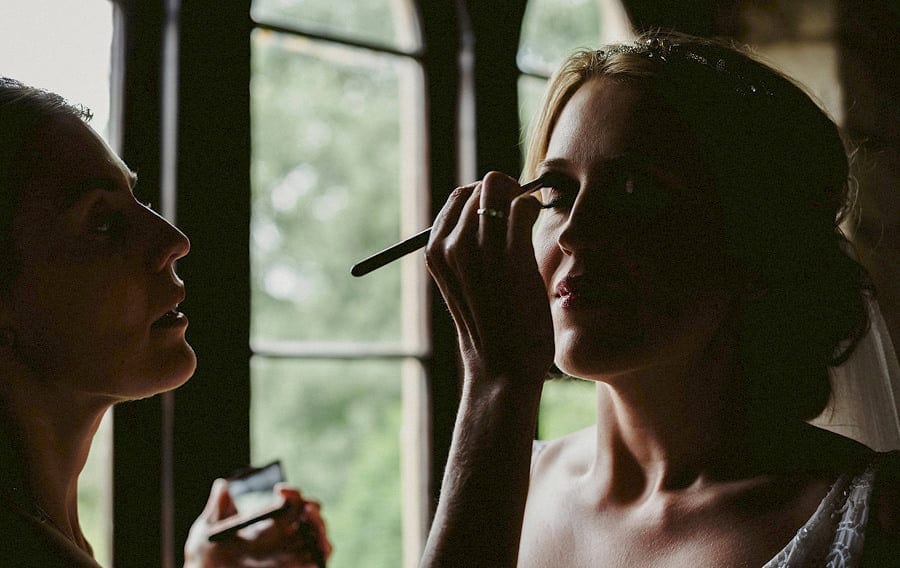 The makeup artist brushes mascara onto the brides right eyelid in the old barn at Childerley
