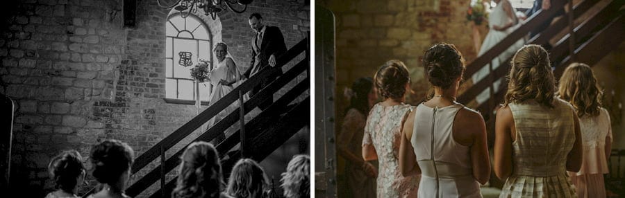 The bride walks down the wooden staircase in the old barn as the bridesmaids stand and watch