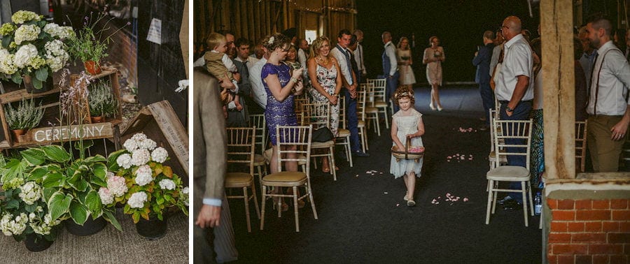 A flower girl walks down the aisle at the old barn in Chelderley and drops petals from a wicker basket