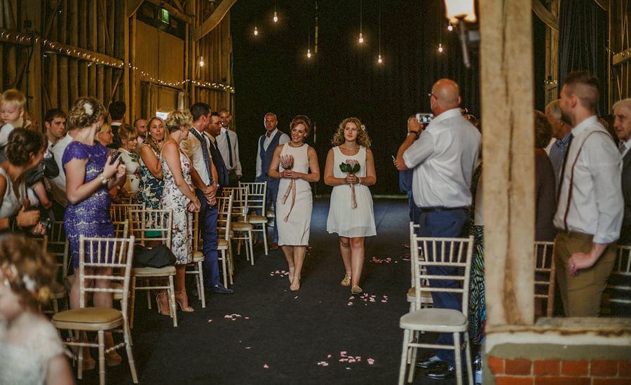 Two bridesmaids walk side by side down the aisle in the old barn at Childerley Estate in Cambridgeshire