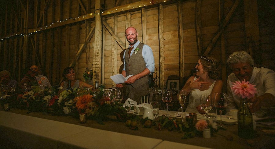 The groom smiles as he stands in front of wedding guests and delivers his speech in the old barn at Childerley