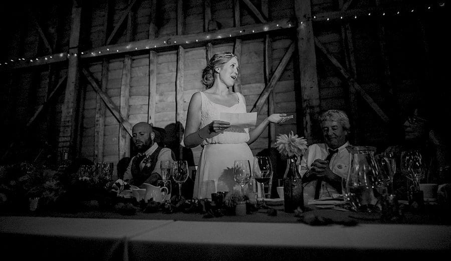 The bride stands in front of wedding guests and delivers her speech in the old barn