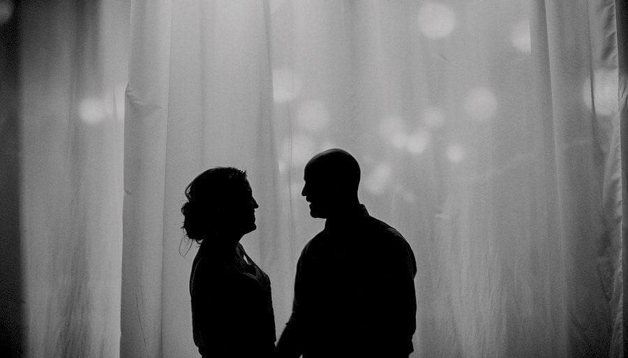 The bride and groom look at each other and stand next to a large net curtain in the old barn at Childerley