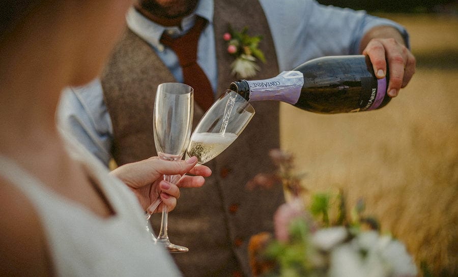 The groom pours champagne into glass flutes held by the bride