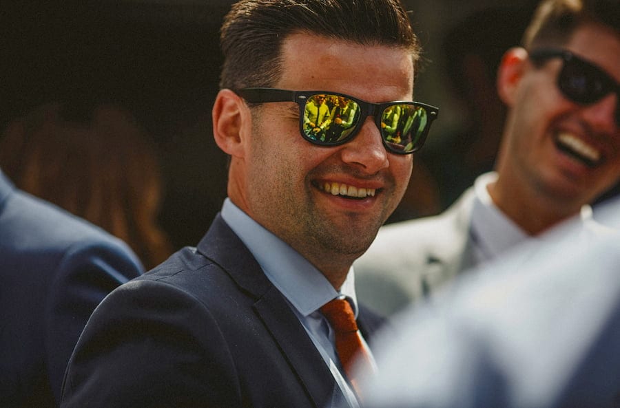 A man with sunglasses smiles at the bride and groom
