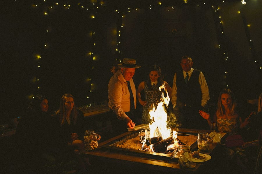 Wedding guests gather around the fire pit to toast marshmallows in the tipi