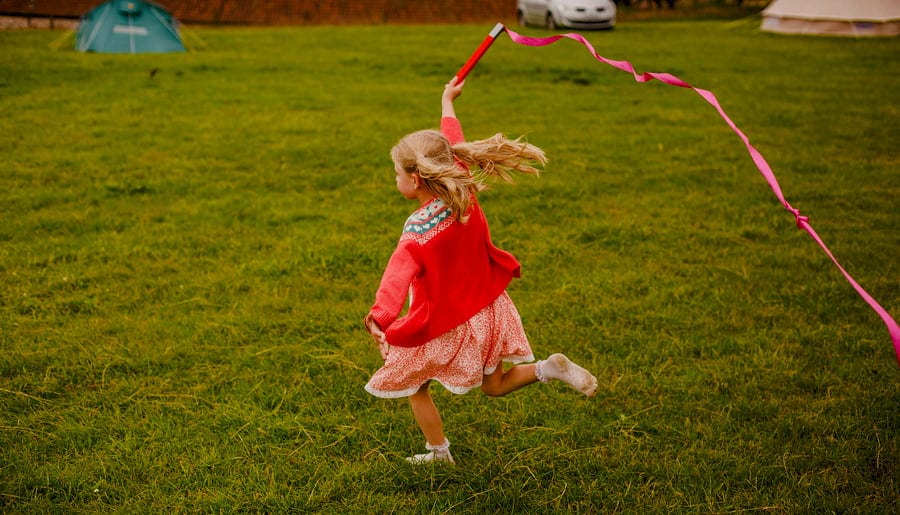 A girl runs through a field at Fernhill Farm carrying a long red ribbon through the air