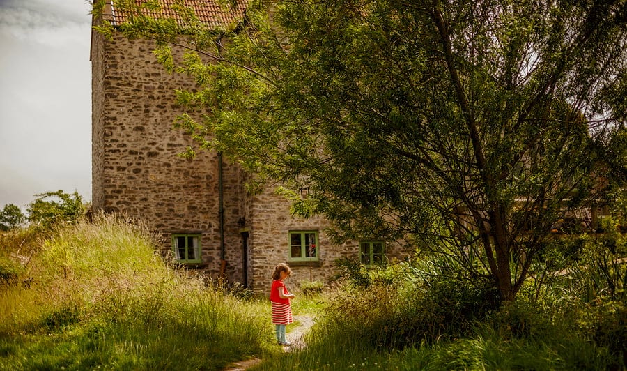 A little girl waits on her own outside the cottage at Fernhill Farm in Somerset