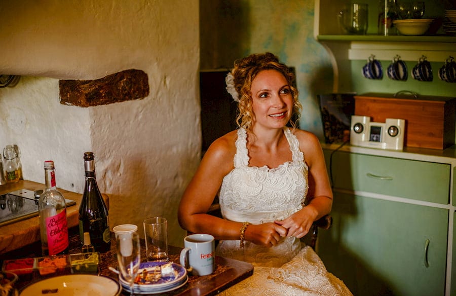 The bride sits at a wooden table in the kitchen of the cottage