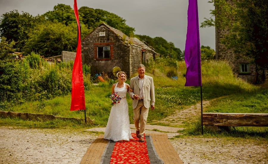 The bride and her Father walk towards the outdoor wedding ceremony at Fernhill Farm in Somerset