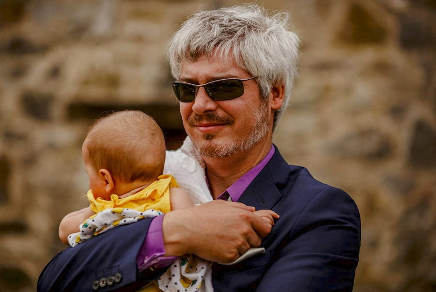 A wedding guest holds his baby in his arms and listens to the wedding ceremony