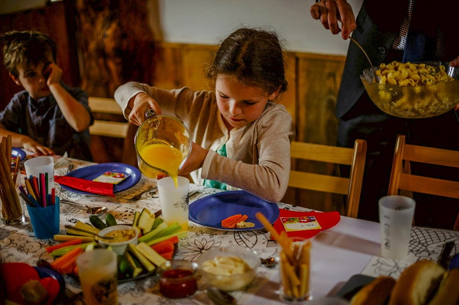 A girl sits at the wedding table and pours orange juice into a plastic cup in the barn