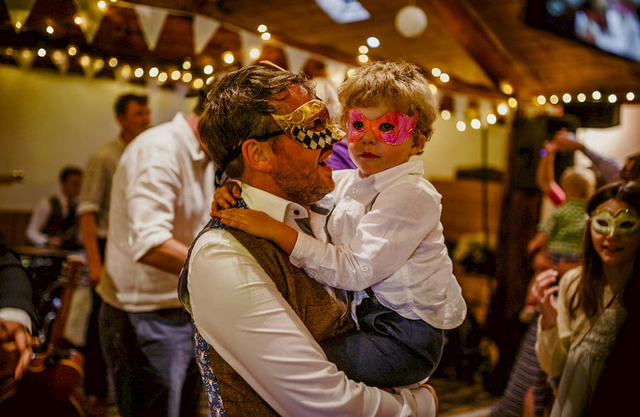 The groom holds his son in his arms on the dancefloor in the barn at Fernhill Farm