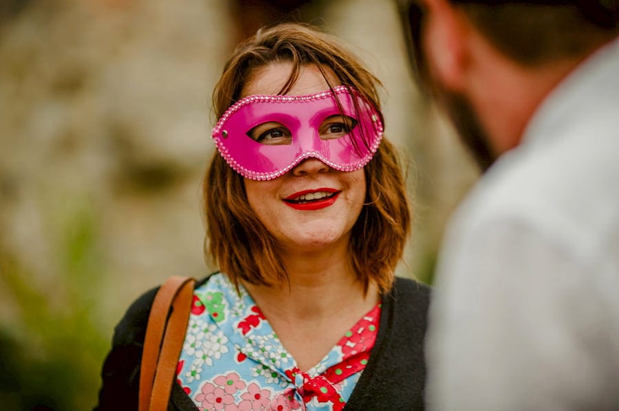 A wedding guest wears a pink mask and chats to a friend in the courtyard