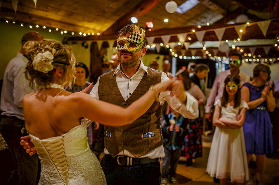 The bride and groom wear masks and dance in the barn at Fernhill Farm