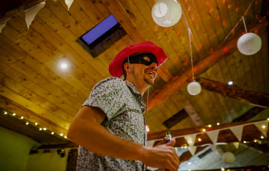 A wedding guest wearing a red hat and black face mask dancing in the barn at Fernhill Farm