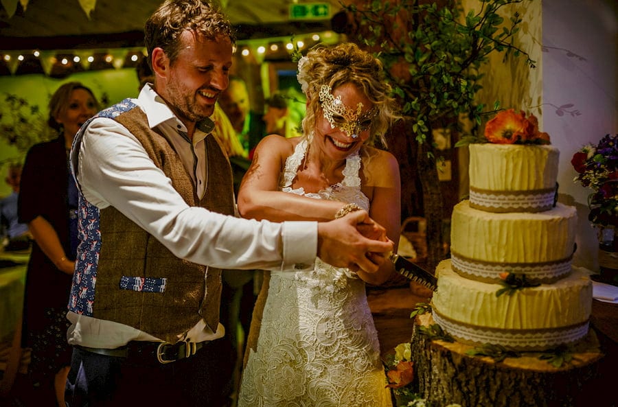 The bride and groom stand next to each other and cut the cake in the barn