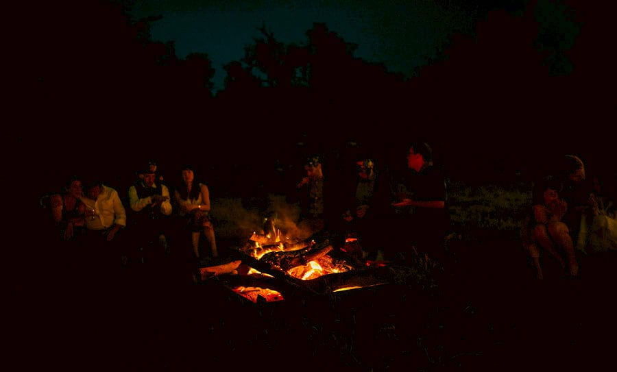 Wedding guests sit around an open fire in the courtyard at Fernhill Farm