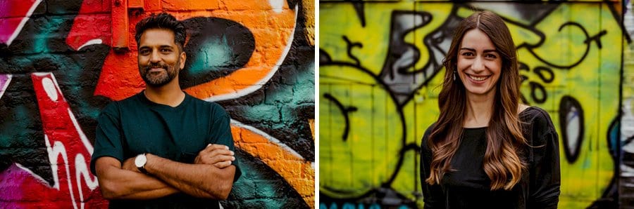 A man and lady pose for a photograph against a multi coloured wall