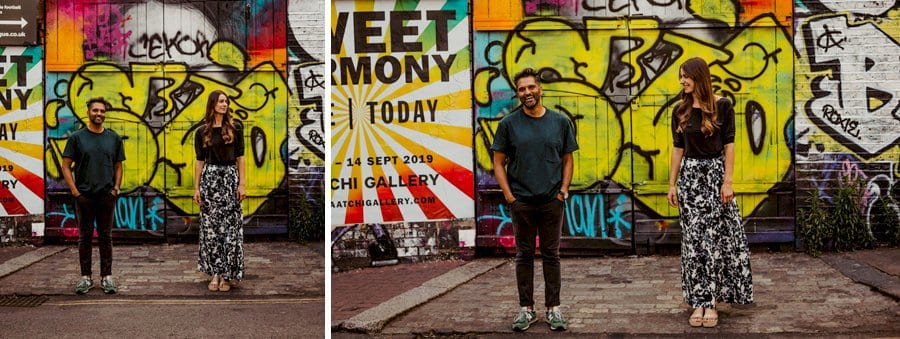 A lady and a man stand against a kerb and laugh with each other as they pose for a photograph