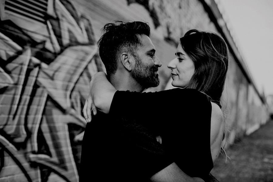 A lady embraces a man and looks into his eyes as the man smiles