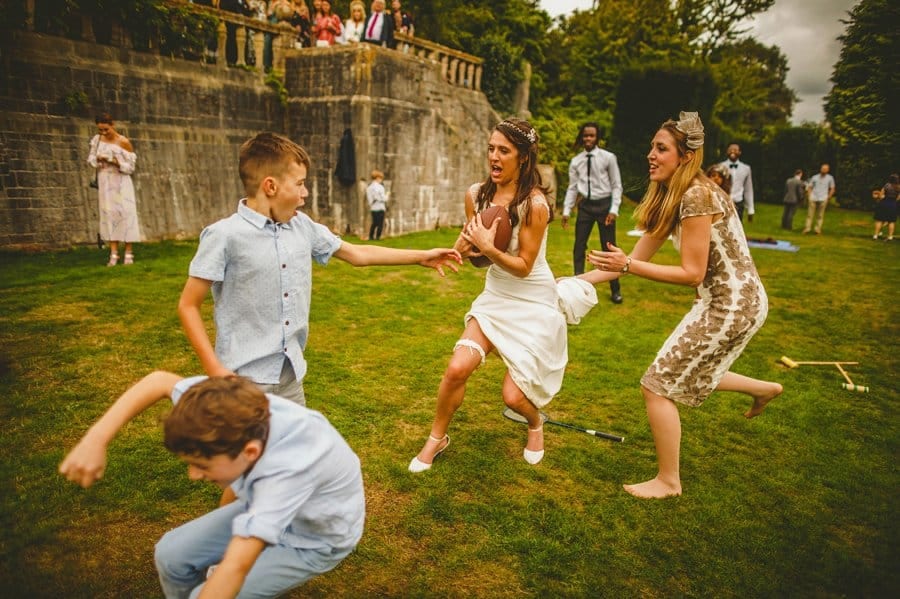 A bride runs across a lawn with wedding guests holding an American football