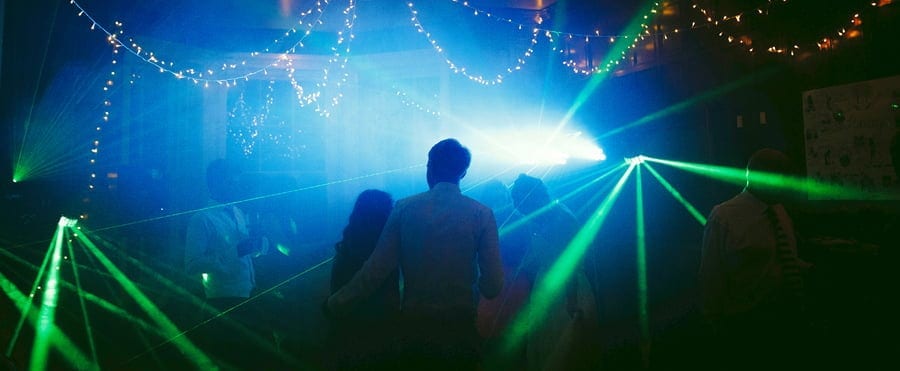 The bride and groom stand next to each other on the dancefloor of the marquee and watch people dancing