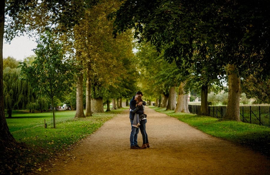 A lady and a man embrace each other as they stand in the middle of a path in a park in Oxford