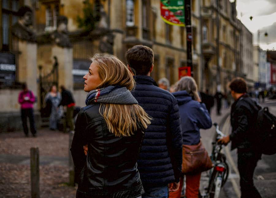A lady walks behind a man in the city centre of Oxford