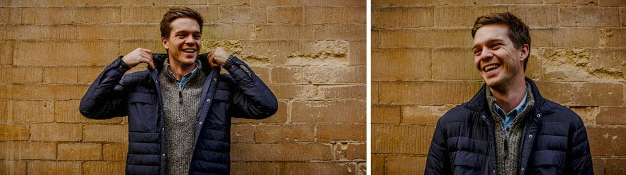 A man lifts the collar of his coat up and laughs against a wall in Oxford town centre