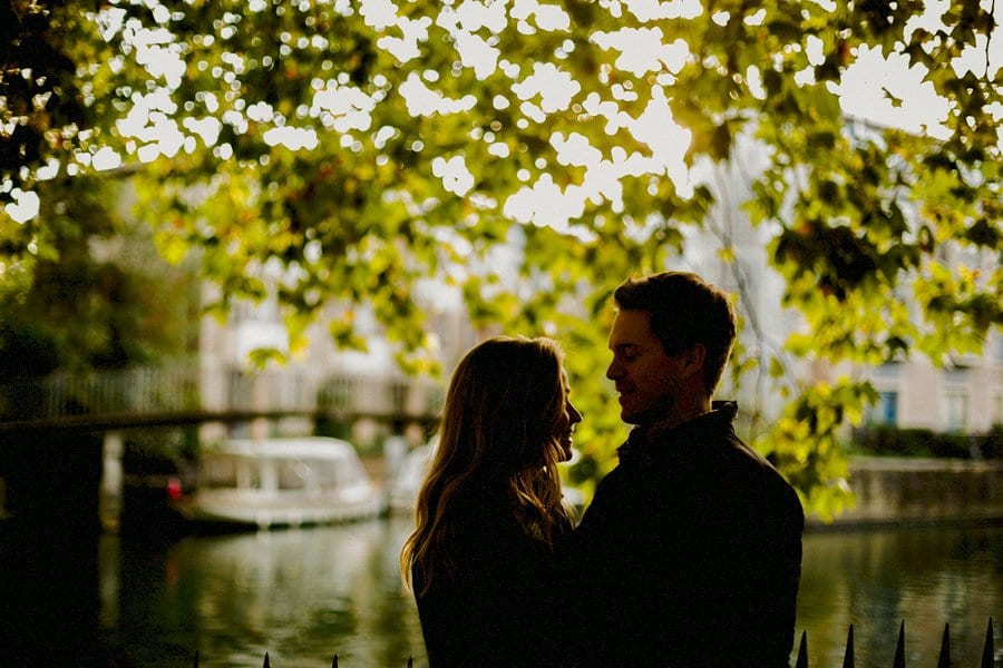 A lady and a man look face to face at each other under a tree next to a canal in Oxford town centre